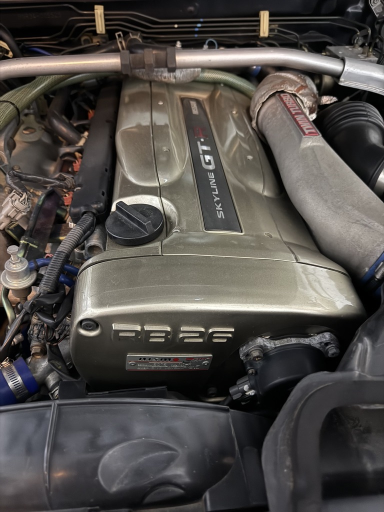 RB26DETT engine bay of the R34 GT-R showing the Skyline GT-R cam cover, RB26 plenum and NISMO-badged plate.